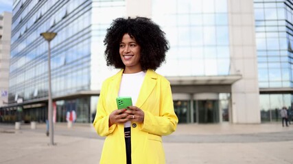 Confident businesswoman working on smartphone, standing near sleek skyscrapers with professional urban cityscape behind her - Powered by Adobe