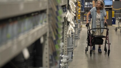An elderly woman uses a walker while shopping at a hardware store, looking for paint to use in her home decorating project and planning restoration details.