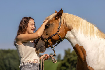 Young woman bonding with Haflinger crossbreed pinto mare outdoors in summer