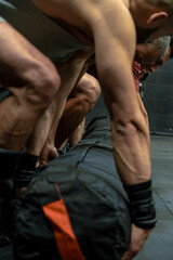 Obraz premium Men doing a CrossFit routine, lifting a heavy sandbag, working as a team in a CrossFit gym. Concept of exercise, gymnastics, sports, health, and wellness.
