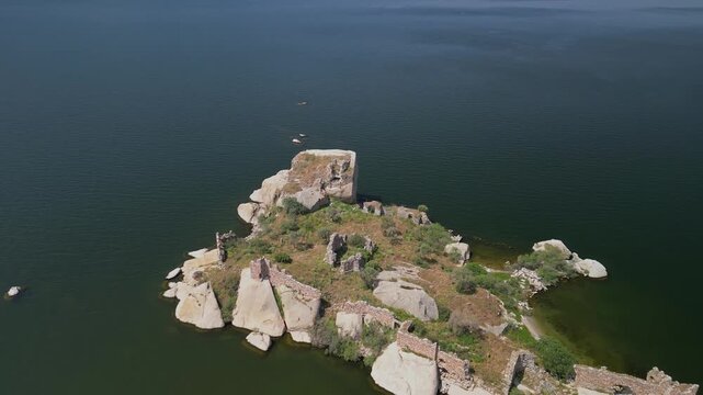Rocky islet with ruined structures sits in Lake Bafa, Turkey. Greenery grows between stones. Drone captures Turkey's forgotten heritage in peaceful lake surroundings. Turkiye view.