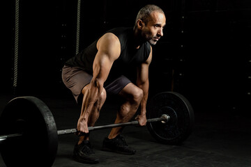 Muscular older Latino man with a barbell and weight plates doing an exercise routine, studio shot....