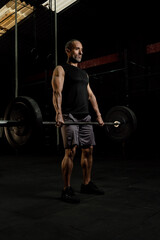 Muscular older Latino man with a barbell and weight plates doing an exercise routine, studio shot....