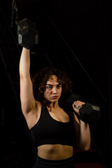 A white Latina woman with curly red hair using weighted dumbbells during her workout routine, studio shot. Concept of exercise, gym, sports, health, and wellness.