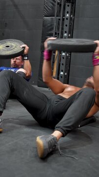 Two men doing sit-ups on the floor with weight plates in a CrossFit gym. Concept of exercise, gymnastics, sports, health, and wellness.