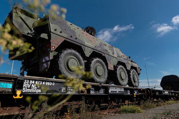 Wheeled armored military vehicle being transported on specialized railroad flatcar