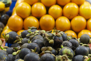 Fresh mangosteens and yellow passion fruits stacked at a market stall.