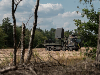 Military radar truck positioned among trees and vegetation for tactical concealment