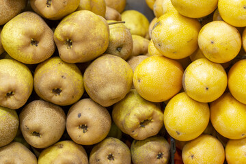 Fresh Asian pears and yellow passion fruits stacked side by side at a market stall.
