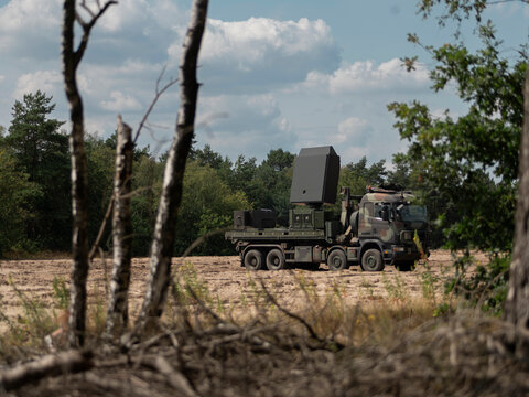Military radar truck positioned among trees and vegetation for tactical concealment - Powered by Adobe