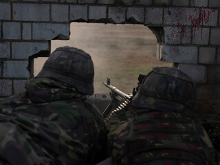 Military personnel positioned at wall breach with machine gun during urban combat exercise