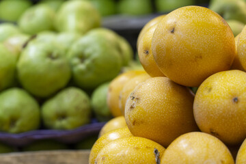 Fresh yellow passion fruits stacked at a market with green guavas in the background.