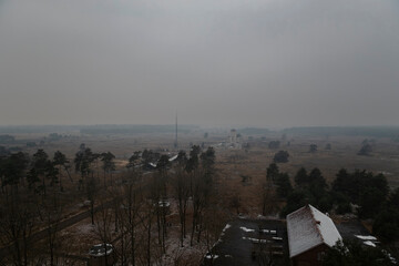 Foggy countryside view with scattered trees and buildings in overcast weather conditions