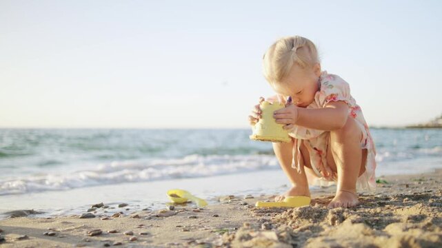 Young child playing on the beach building sandcastles with a yellow bucket during the late afternoon sun