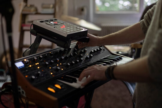 Hands on synthesizer with drum machine in home studio setting