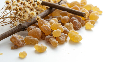 A close up shot of frankincense resin with a small branch and dried flowers on a white background