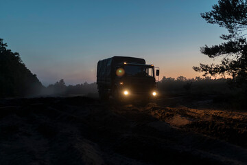 Close-up view of military truck with bright headlights during evening operations in rural forest setting