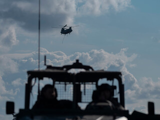 View from military vehicle showing Chinook helicopter flying in distance against cloudy sky