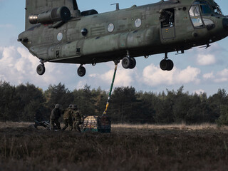 Close view of Chinook helicopter with soldiers preparing cargo for sling load operation on ground