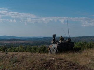 Military vehicle positioned on elevated terrain with soldiers conducting surveillance operations
