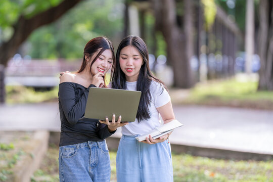 Two young students collaborating on a project using laptop in park - Powered by Adobe