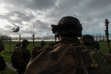 Soldiers observing helicopter approach while positioned in field with dramatic sky