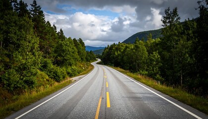 A winding road stretches through a lush forest landscape under a partly cloudy sky.