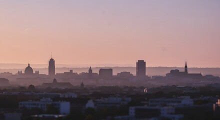 Naklejka premium Hazy Cityscape Silhouette at Sunset with Pastel Plum and Wheat Sky