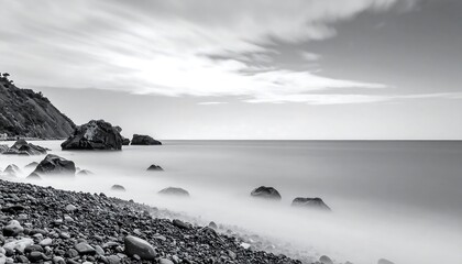 A serene black and white seascape portrays a tranquil coastline with smooth, dark rocks gently nestled on a pebble beach.