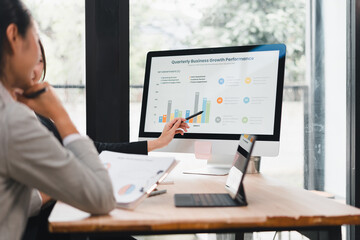 Businesswoman presenting quarterly business growth performance chart on computer screen to colleague in modern office, discussing data analysis and strategy planning