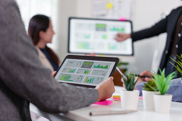 Business team meeting in modern office, person holding tablet with financial data and ESG charts, colleagues discussing analytics on screen, teamwork, sustainability, and technology concept