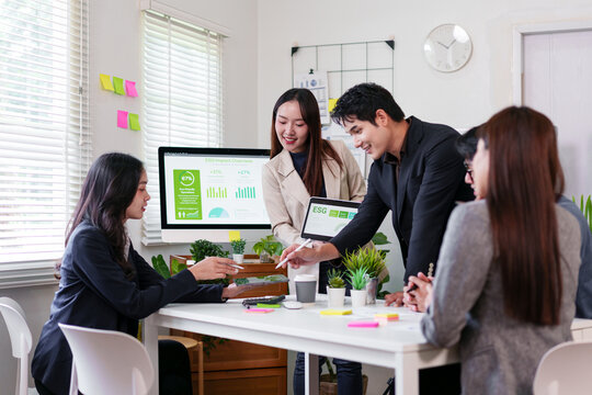 Young professionals discussing ESG impact report in modern office with plants and digital charts, showing collaboration and positive teamwork atmosphere