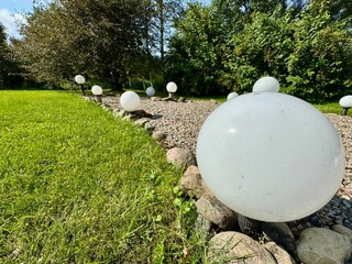 White spherical garden lamps placed along a gravel path on green summer lawn