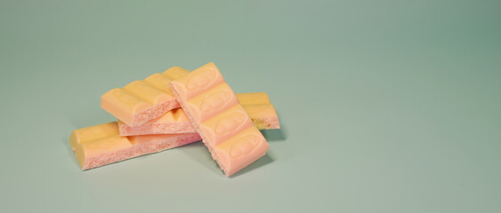 A stack of strawberry flavored milk chocolate bars with bubbly texture on a pastel mint green background, symbolizing sweet dessert, confectionery and snack concept. copy space