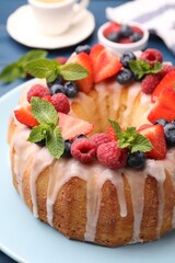 Delicious bundt cake with berries, glaze and mint on blue table, closeup
