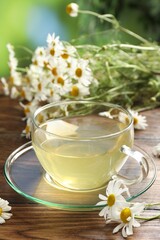 Tasty chamomile tea and flowers on wooden table, closeup