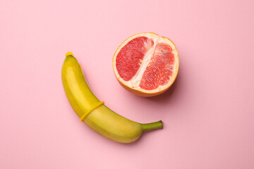 Sex education. Banana with condom and grapefruit on pink background, top view