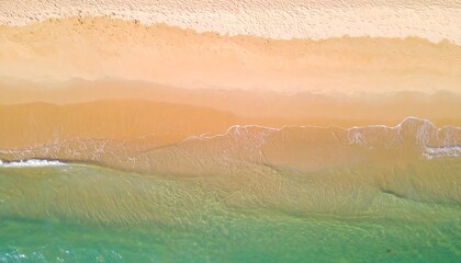 High-angle view of a beach shoreline with gentle waves lapping the shore, displaying a spectrum of warm sand colors and turquoise water.