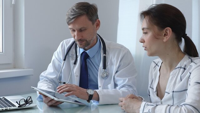 Doctor showing information on a digital tablet to a patient during a medical consultation in a bright office, discussing diagnosis and treatment options. Medicine and health care - Powered by Adobe