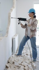 Female construction worker demolishing a wall with a hammer drill, wearing protective gear,...