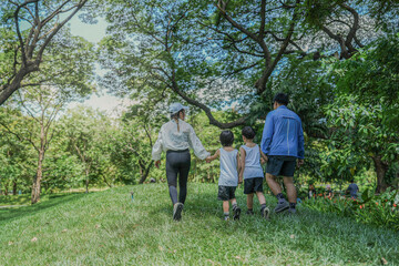 Rear view of a happy Asian family on a weekend outing. Parents and two sons hold hands, walking up...