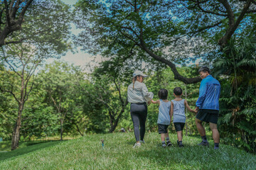 A happy Asian family with two young sons enjoys a walk in the park. Parents hold their children's hands while exploring a lush green hill together, a concept of family bonding.