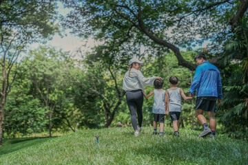 Fototapeta premium A beautiful moment of parenting. An Asian mother and father guide their two young sons by the hand up a green hill, creating cherished childhood memories in a beautiful park setting.