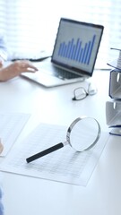 Close up of magnify glass over financial documents near blue folders full of financial papers,...