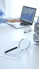Close up of magnify glass over financial documents near blue folders full of financial papers,...