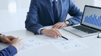 Business colleagues or partners are discussing financial data on a laptop and printed documents while analyzing charts and market trends at office table. Businesspeople and finance concept