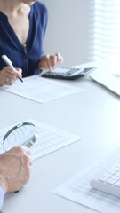 Two professional accountants analyzing financial reports with magnifying glass and calculator, performing accounting and auditing tasks in the office, close up of hands. Audit and taxes in business