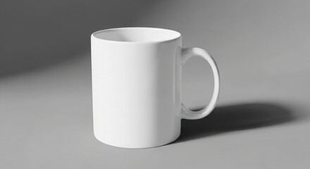 Obraz premium A simple white ceramic mug with a handle sitting on a gray surface in a studio setting with soft lighting