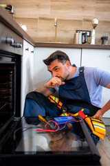 Repair technician inspects oven components in modern kitchen setting with tools nearby