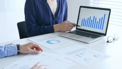 Business professionals collaborating on a laptop, reviewing financial documents, and discussing project strategies in a modern office. Businesspeople in finance concept
